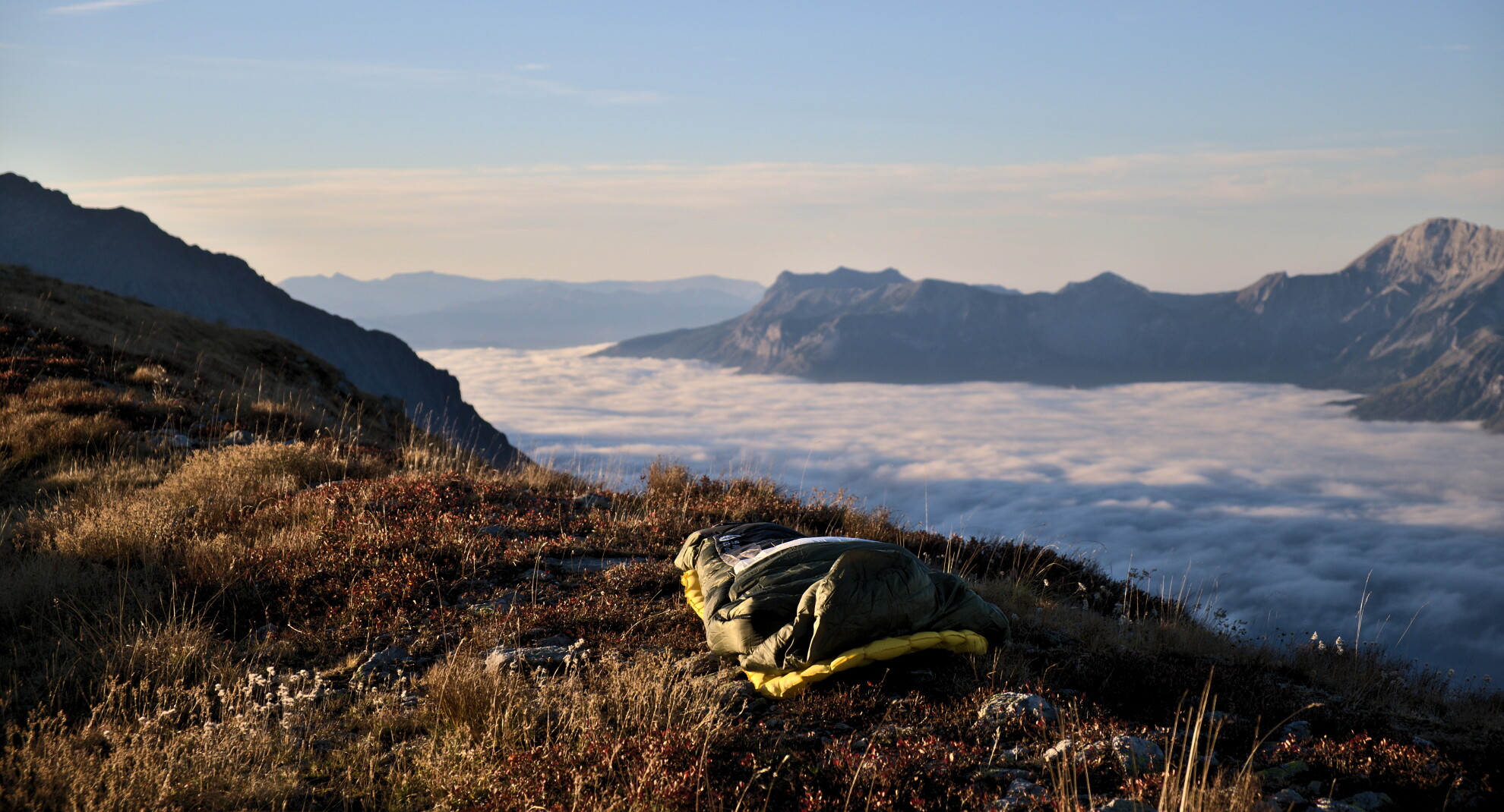 Sleeping bag laid out on a grassy shoulder above a sea of cloud